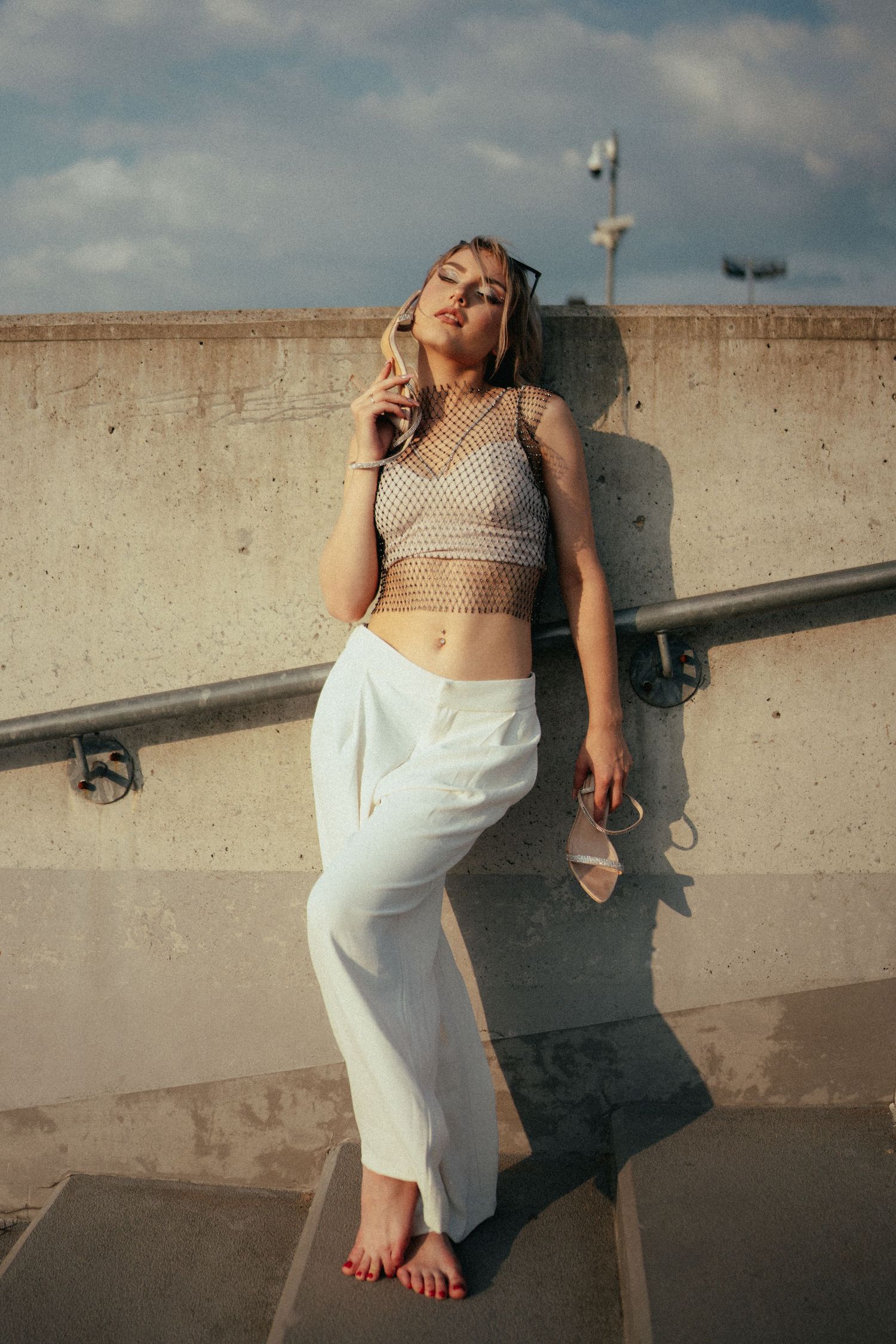 Artistic series of a person in white skirt and crop top posing against a concrete wall in sunlight.