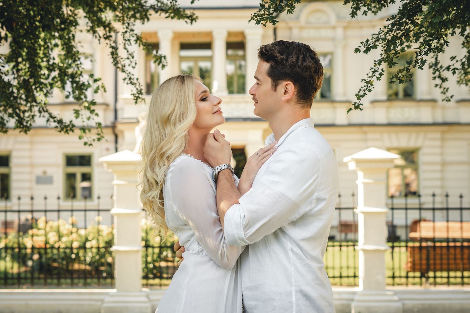 A couple shares romantic kisses in a series of outdoor photos with elegant architecture and greenery in the background.