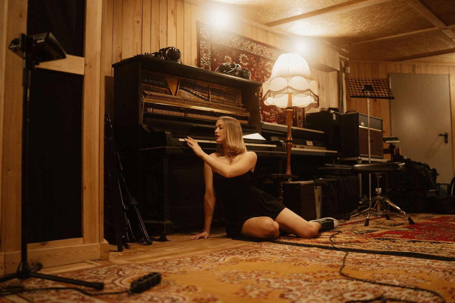 A dancer stretches in a warmly lit studio with a piano and oriental rug creating an artistic atmosphere.