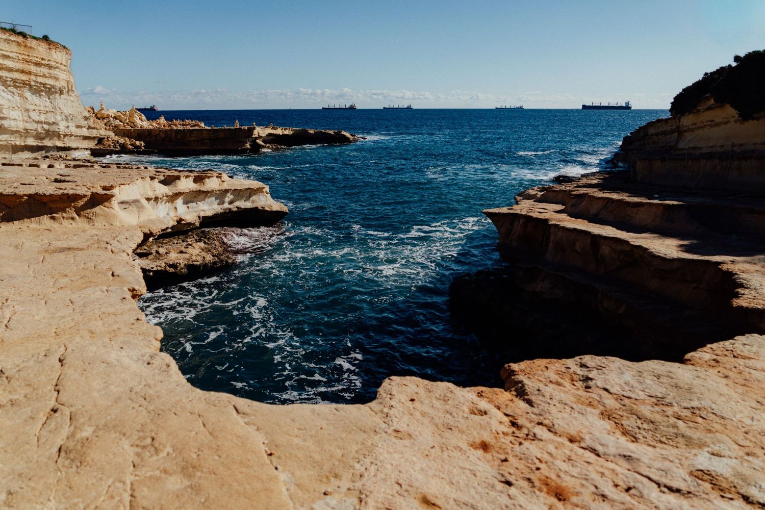 Rocky coastal formation with deep blue Mediterranean waters crashing against limestone cliffs.