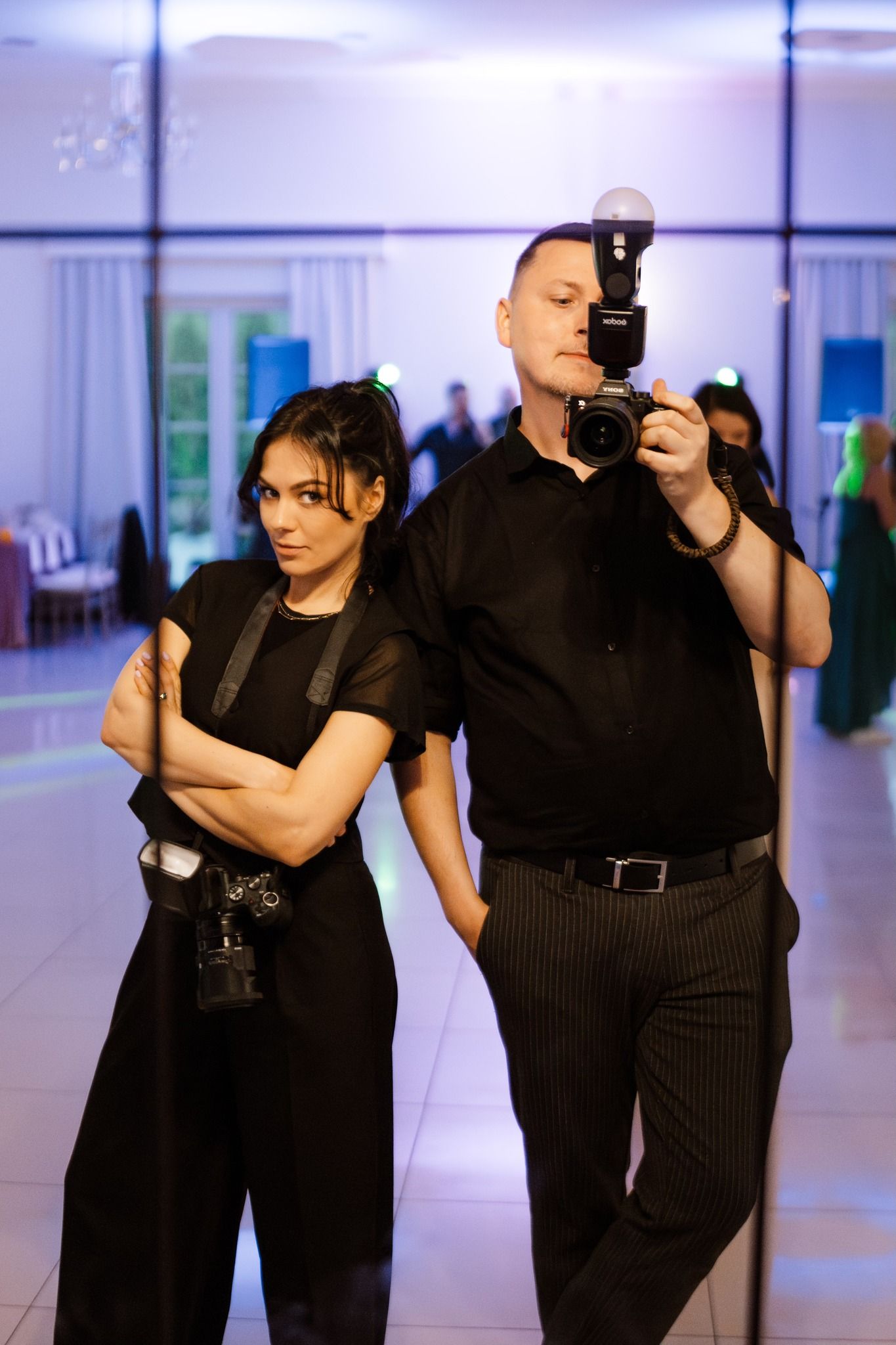 Two dancers in black outfits perform a dramatic dance sequence in a bright studio space.