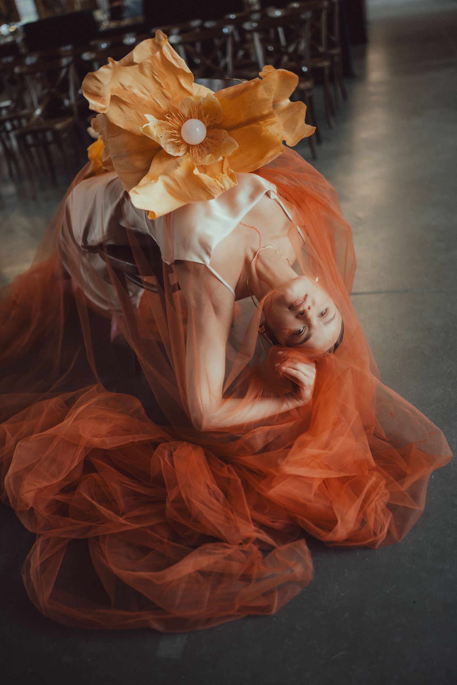 Artistic fashion photo with flowing orange tulle dress and large floral headpiece.