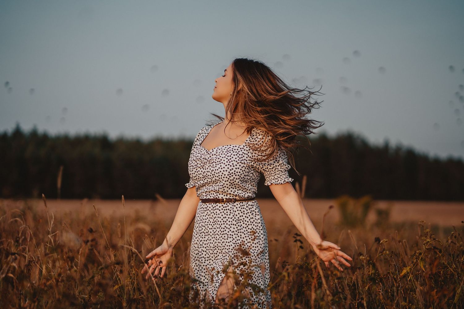 A person in a floral dress spins joyfully in a golden wheat field at sunset.