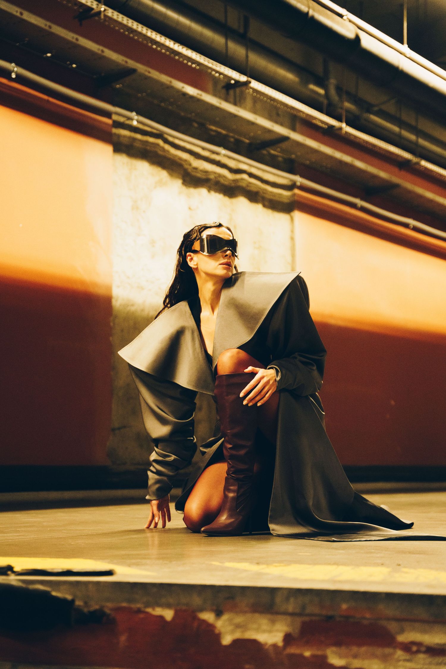 A person in dark clothing crouches on a reflective floor with dramatic lighting creating a moody artistic composition.
