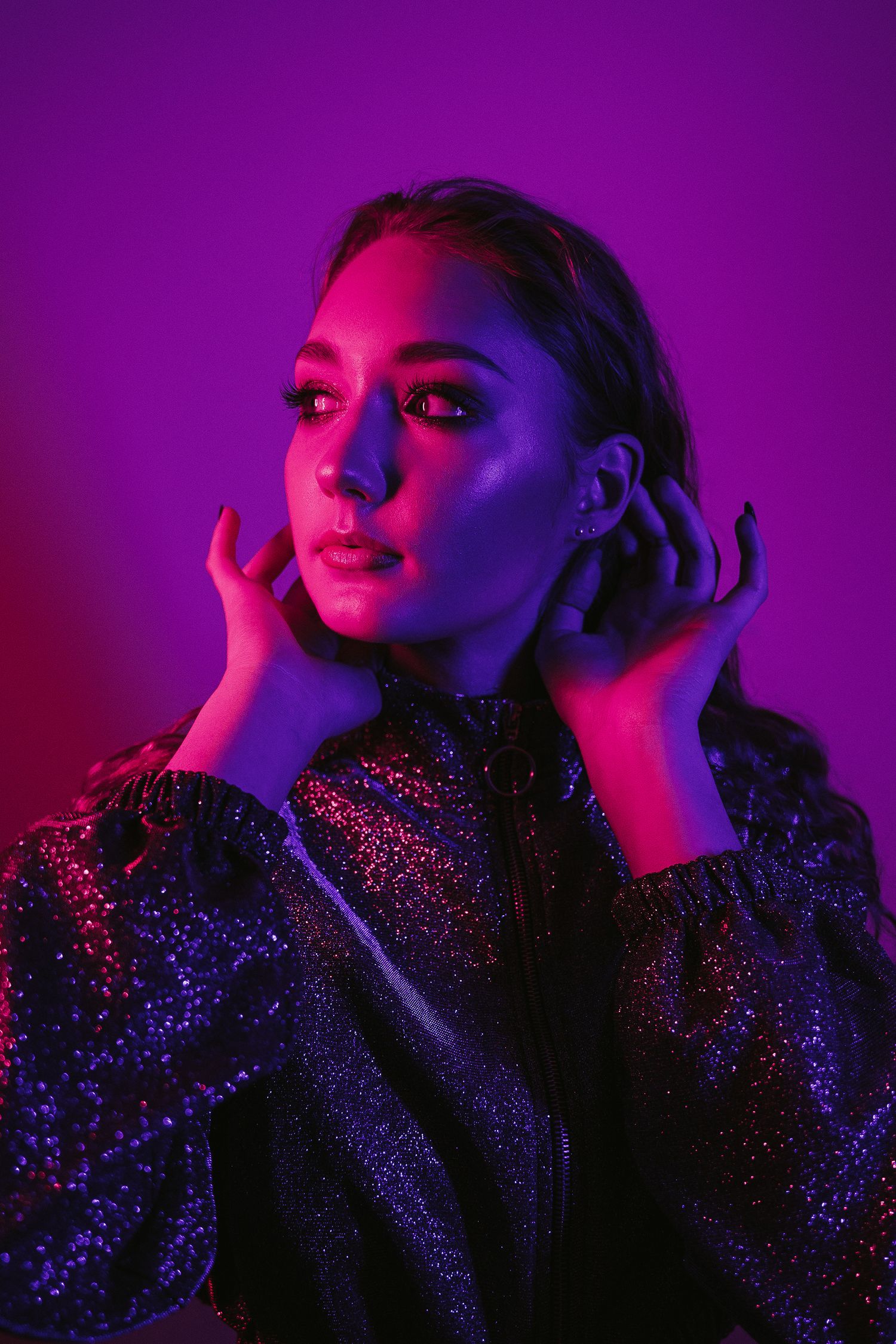 A dramatic fashion portrait with glittering fabric under vibrant purple and red lighting creates a moody aesthetic.