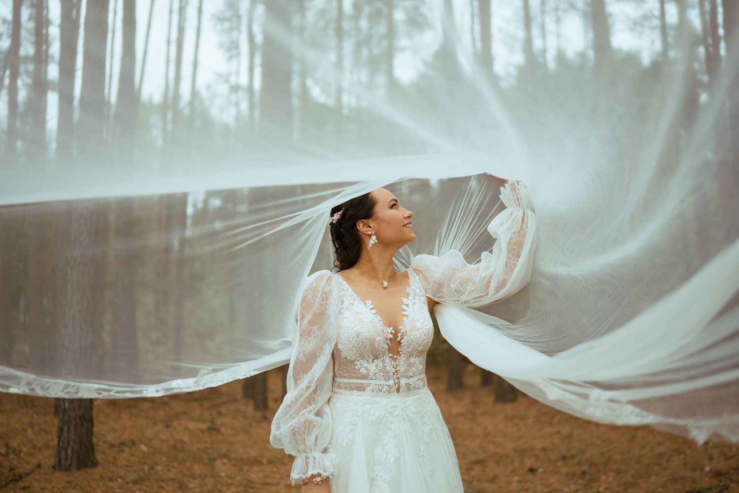 Ethereal bridal portrait with flowing veil in a misty forest setting.