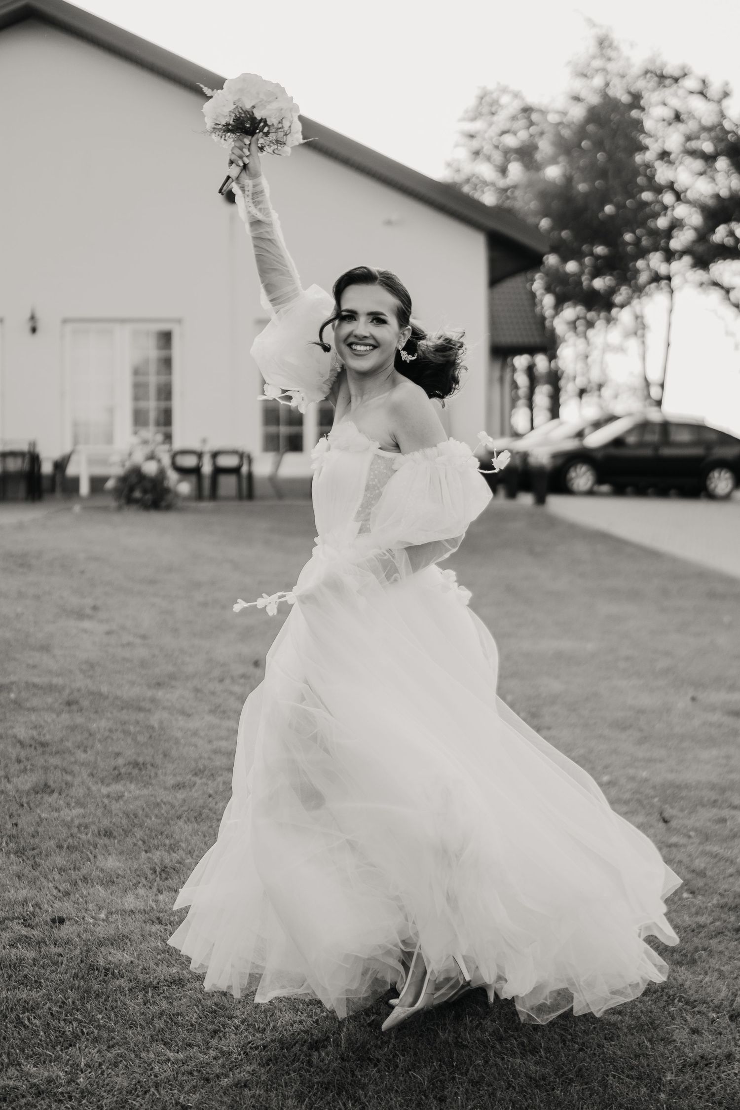 Joyful bride twirling in a flowing white wedding gown on a grassy lawn.