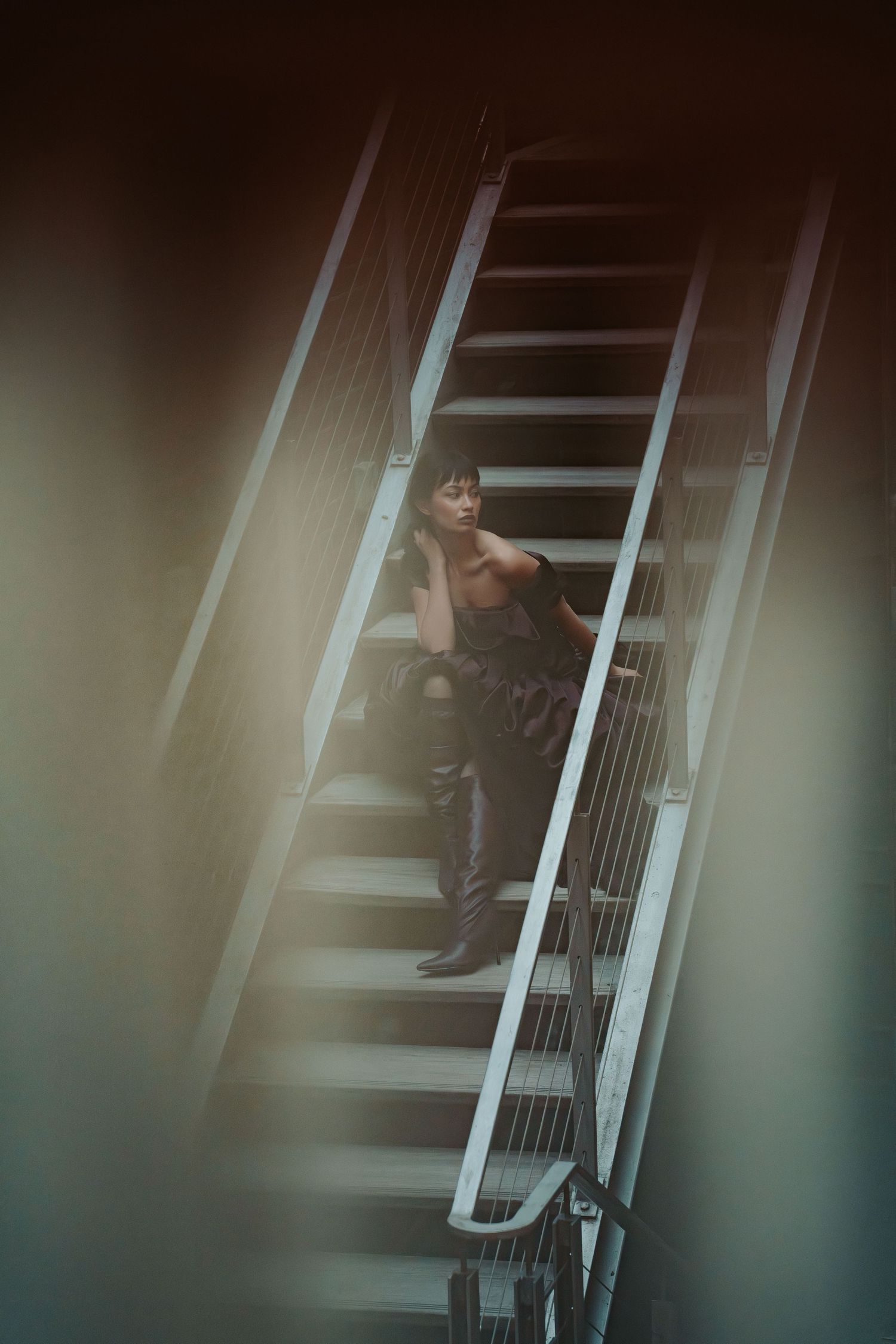 A figure sits on dark moody stairs in an artistic portrait with ethereal lighting and shadows.