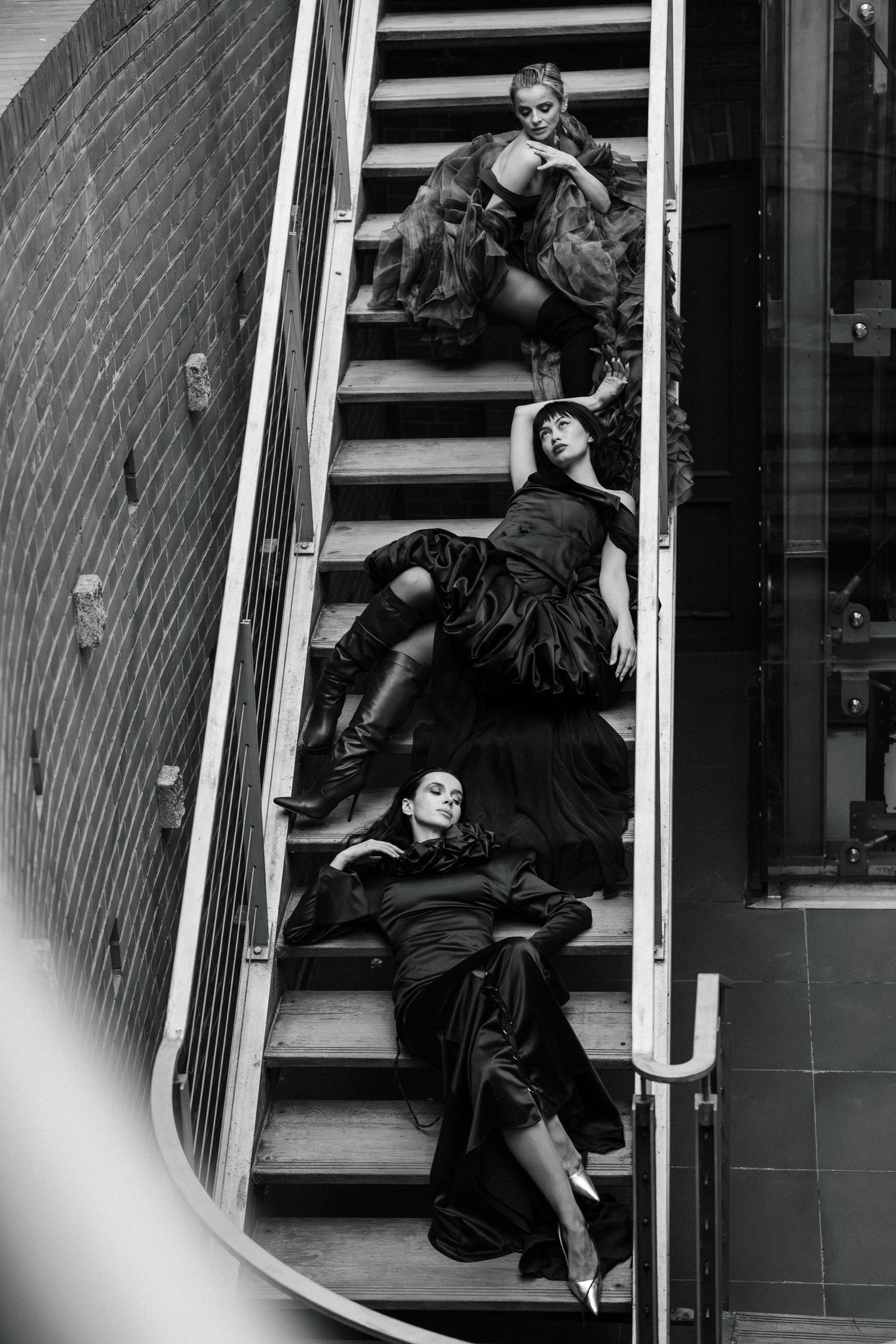 Three performers in dark clothing pose dramatically on curved staircase in black and white artistic photograph.