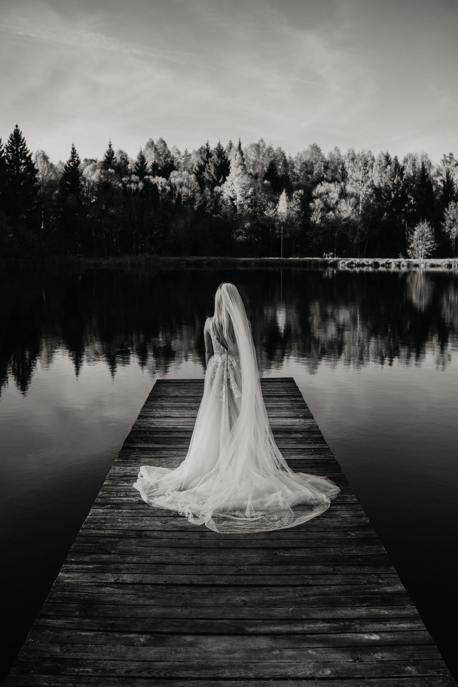 Black and white photos capture a figure in flowing white dress on wooden dock by tranquil lake.