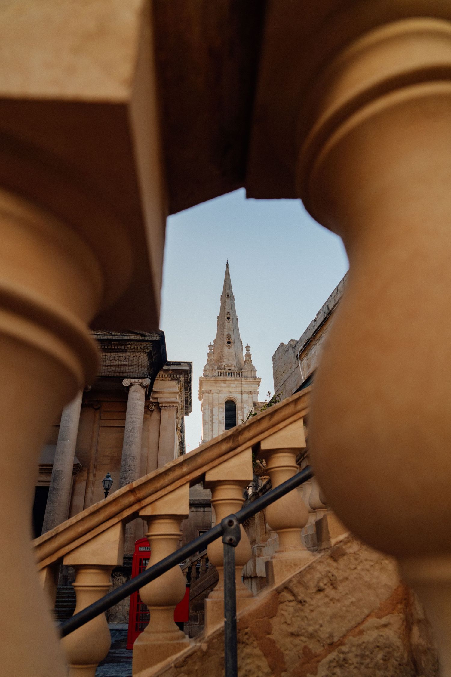 Church spire viewed through architectural columns and archways in warm sandstone.