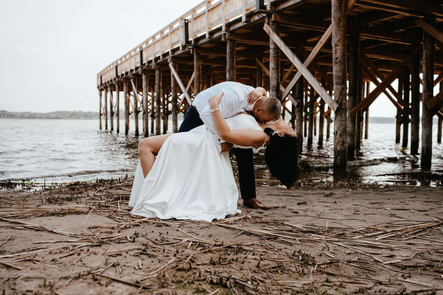 Romantic wedding photo captured on a beach with wooden pier in the background.