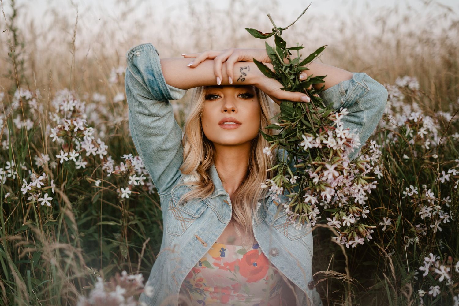 A dreamy outdoor portrait series shows a person in denim against flowering spring blossoms and tall grass.