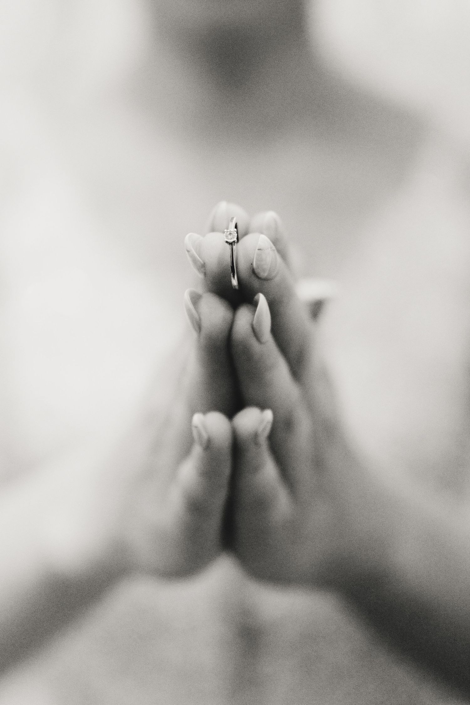 Hands clasped together in prayer position against a soft black and white background with shallow depth of field.