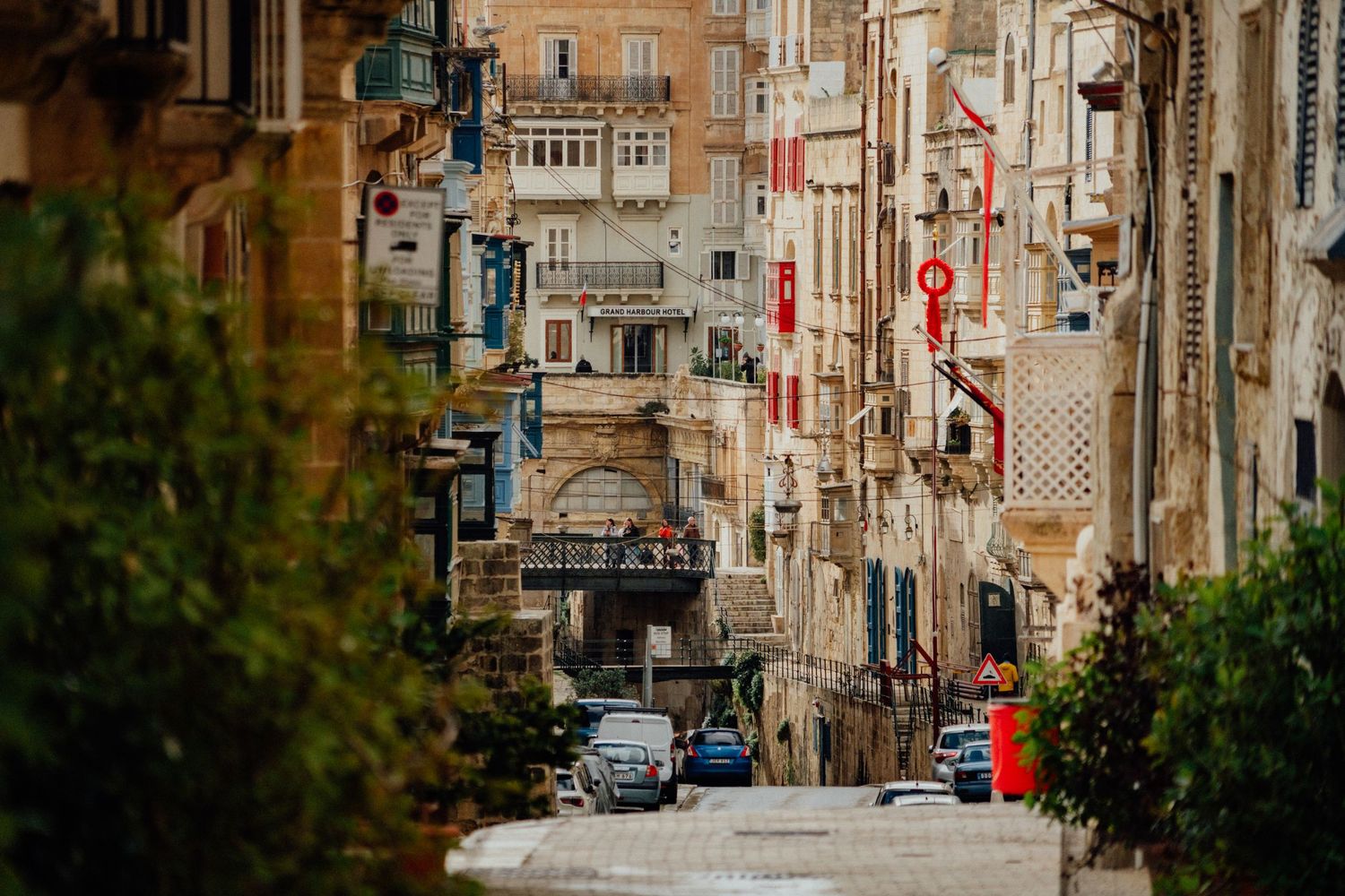Steep urban street in Malta with traditional architecture and parked cars on a hillside.