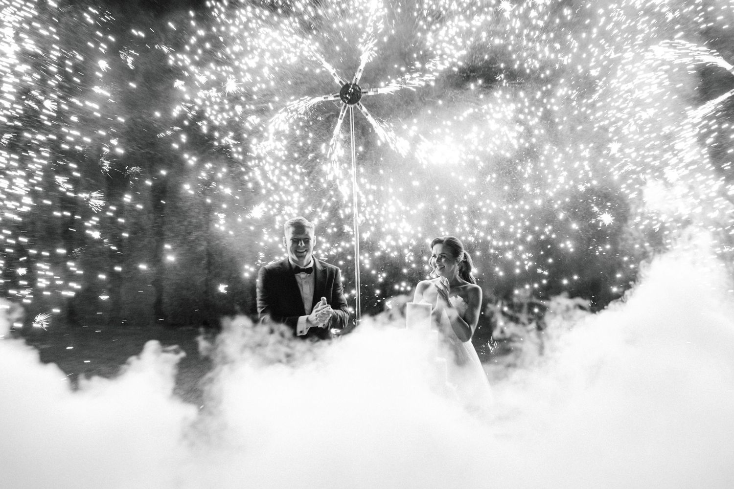Sparklers create magical light trails in a black and white outdoor celebration scene.