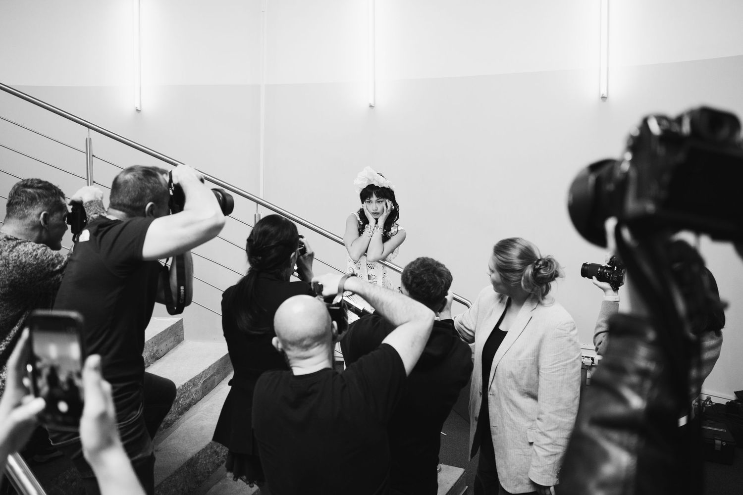 Photographers surround a woman on stairs at a press event in black and white photography.