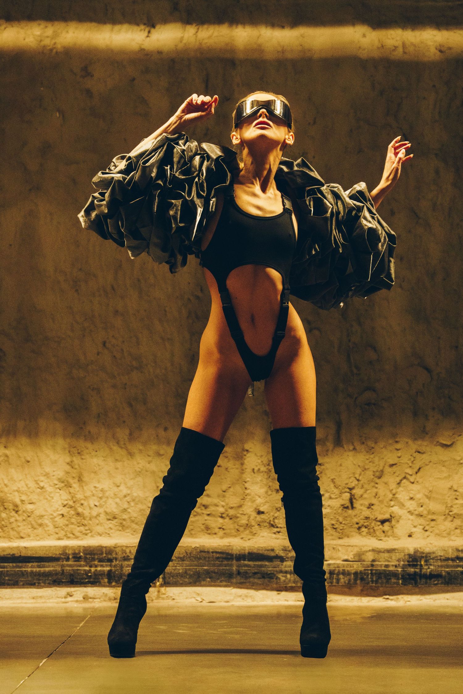 A dancer in denim and black performs a dynamic bending movement sequence against a textured wall in sepia tones.