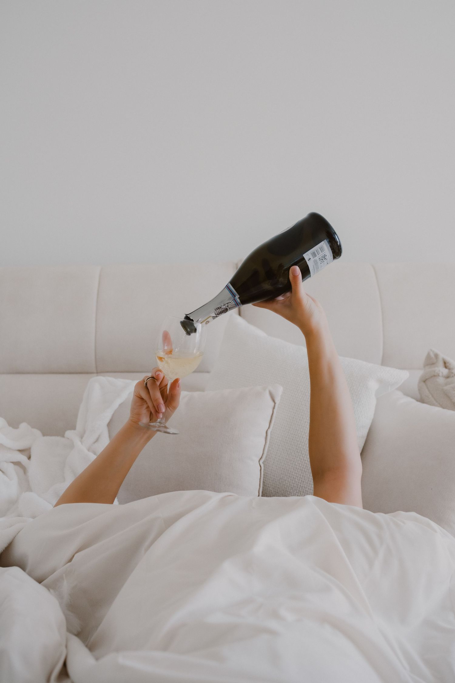 Person relaxing in white bedding while holding a phone or device above them.