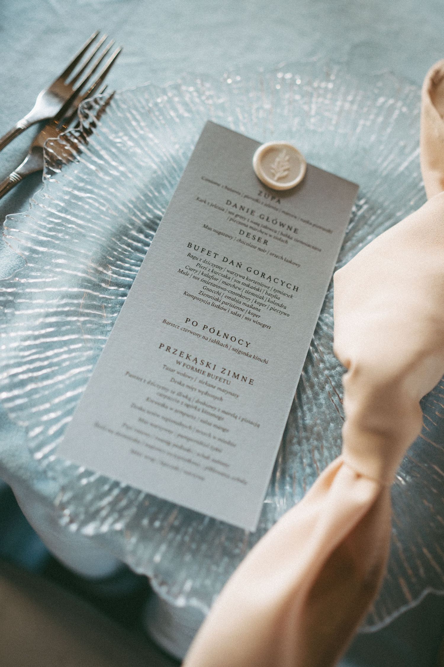 Elegant wedding menu cards displayed on textured glass charger plates with soft blue tones and minimalist typography.