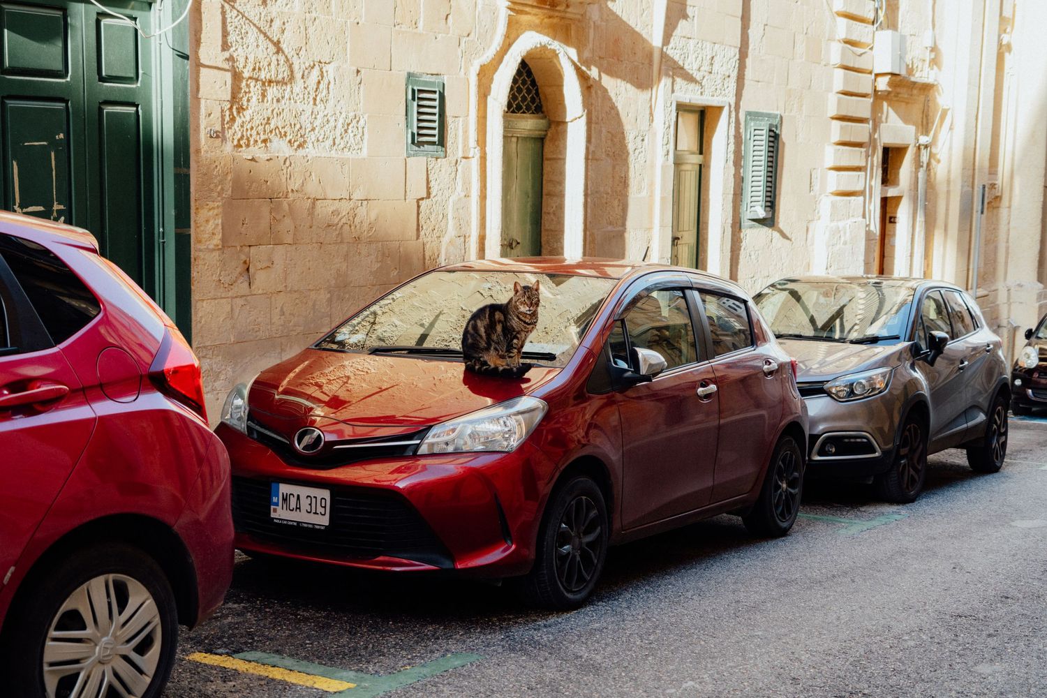 Row of parked cars along narrow street with traditional stone buildings.