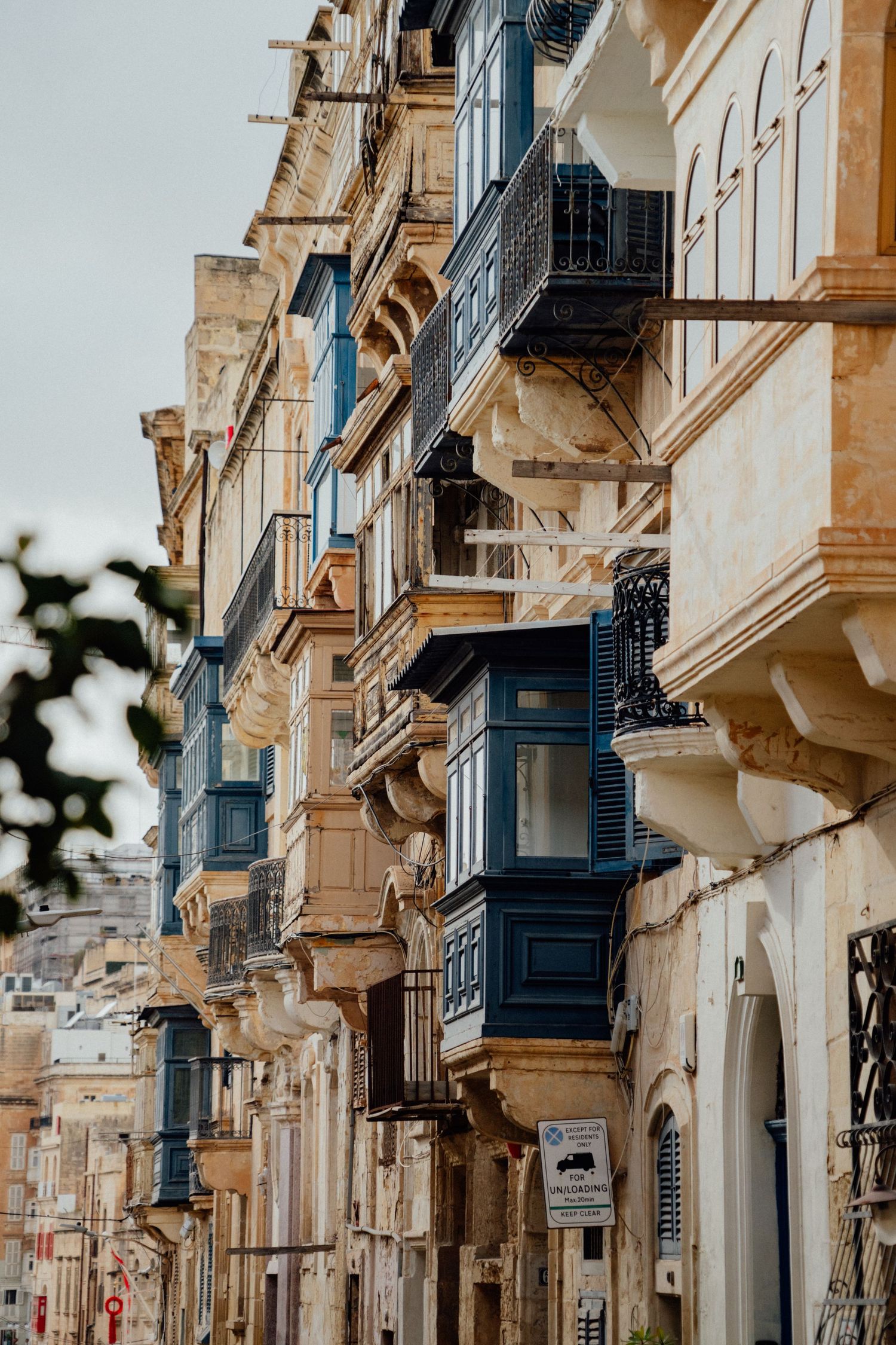 Row of traditional limestone buildings with blue wooden balconies along a street.