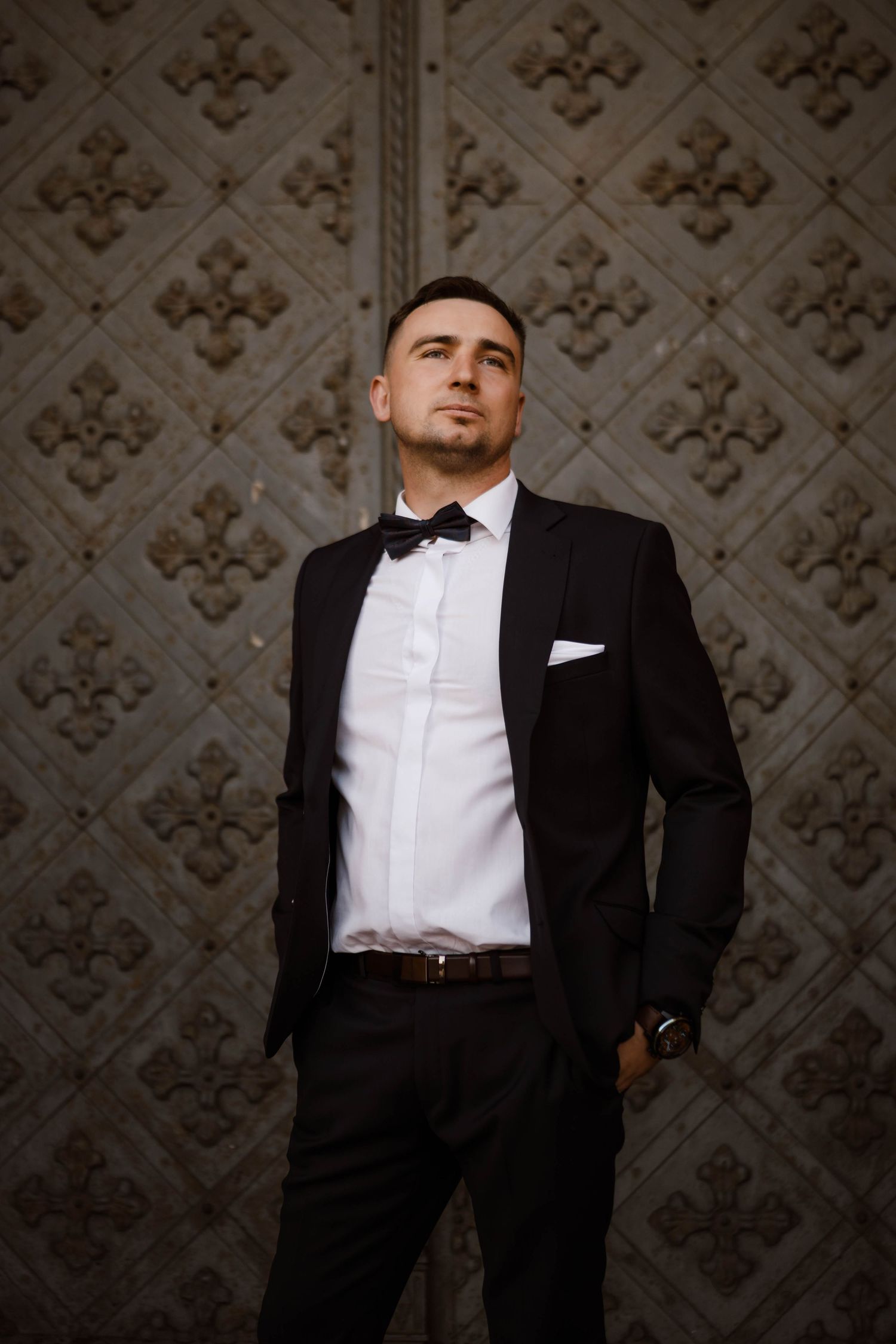 Elegant black tie portrait session against decorative wall background.