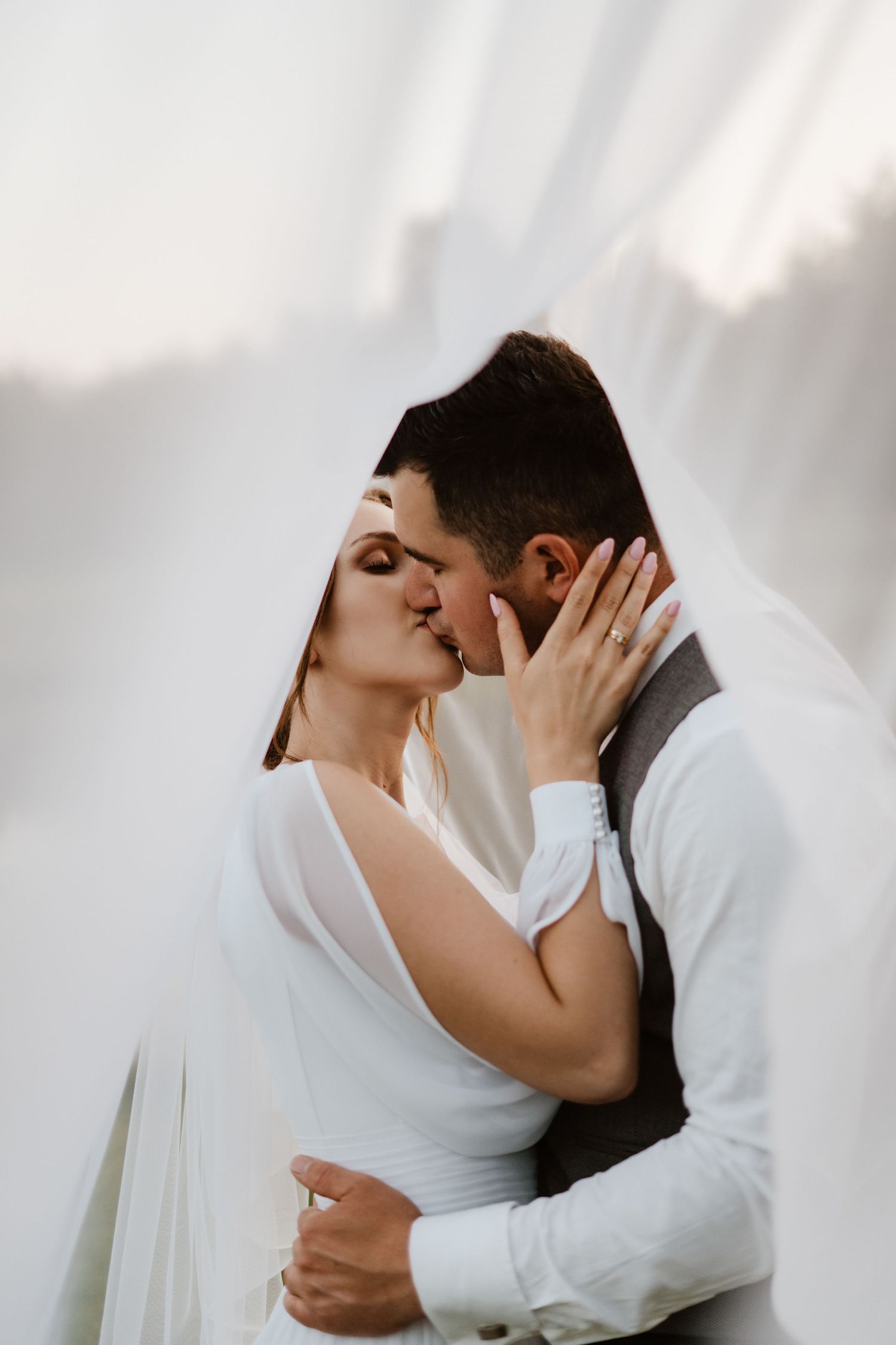 A romantic wedding couple in white attire sharing intimate kisses in a series of four connected photos.