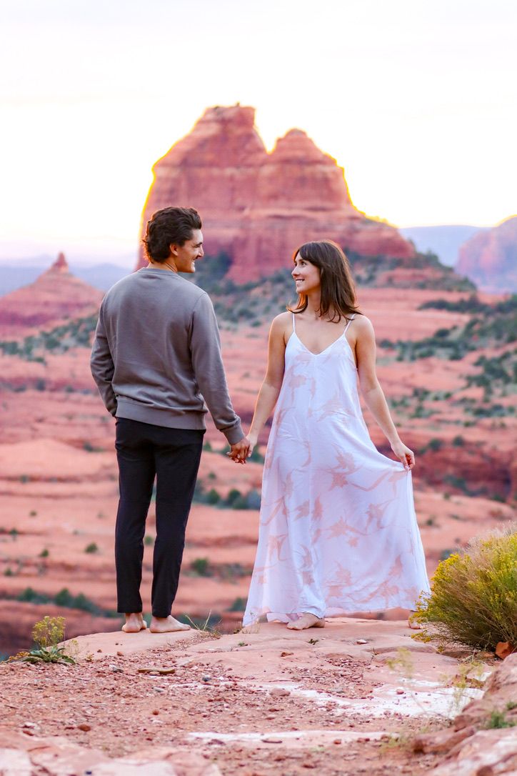 A couple walks along a desert trail with red rock formations in the background during sunset in Sedona Arizona.