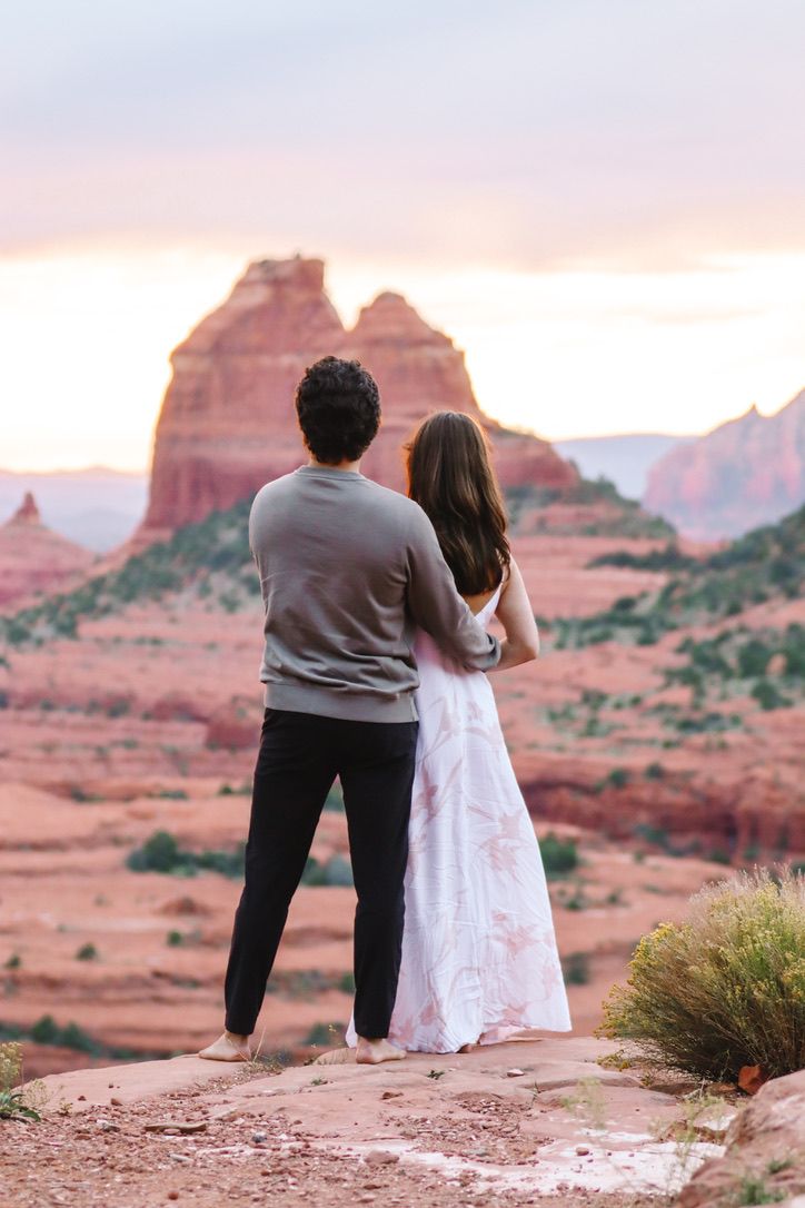 A couple gazes at the sunset over Sedona's iconic red rock formations and desert landscape in Sedona Arizona.
