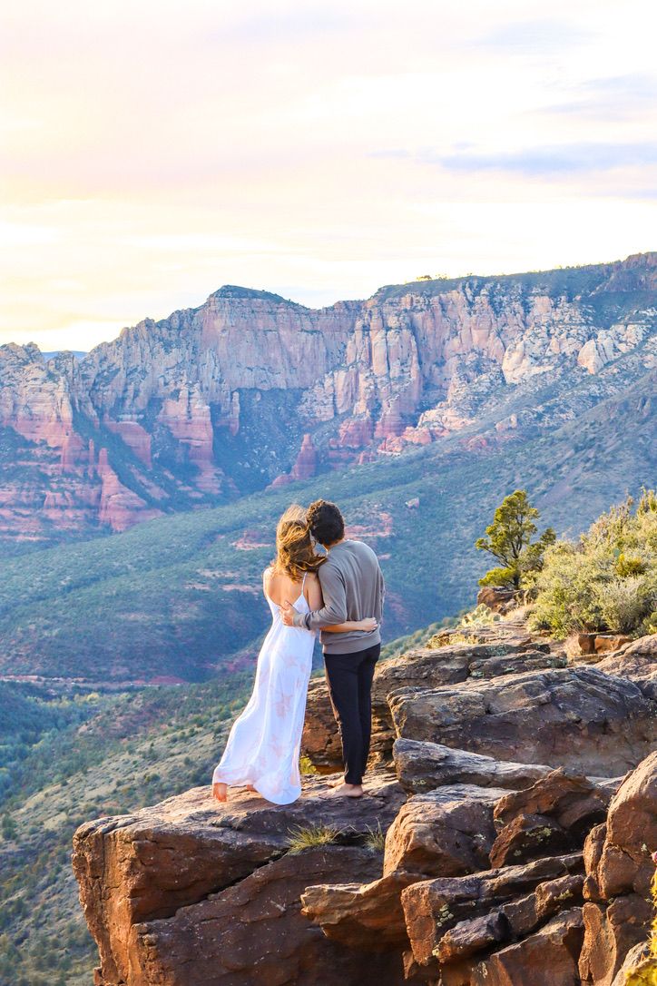 A couple embraces while overlooking a dramatic canyon vista during golden hour in Sedona Arizona.