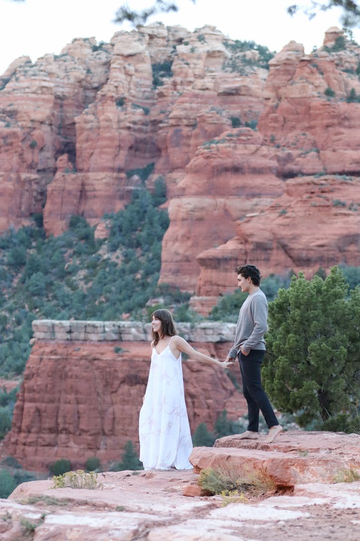 Two people standing on red rocks with majestic sandstone cliffs rising behind them in Sedona.