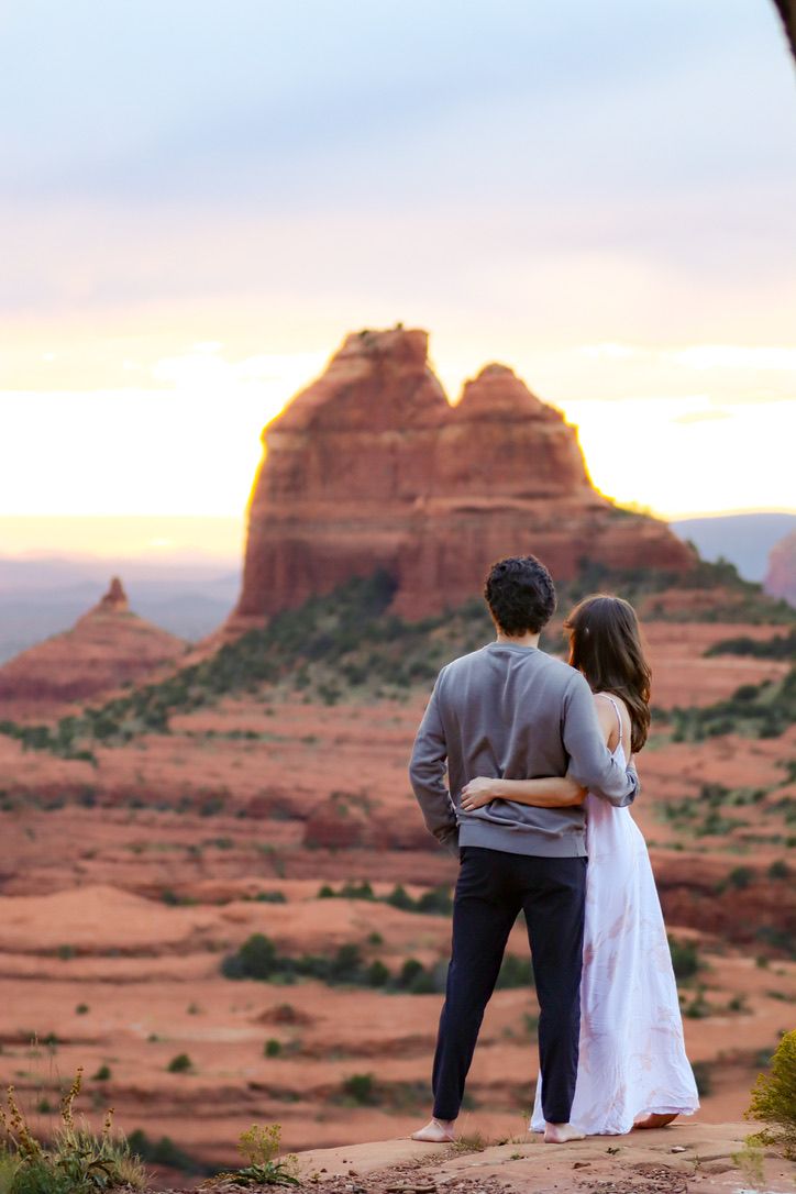 A couple admires the sunset view of Sedona's iconic red rock formation in the desert in Sedona Arizona.