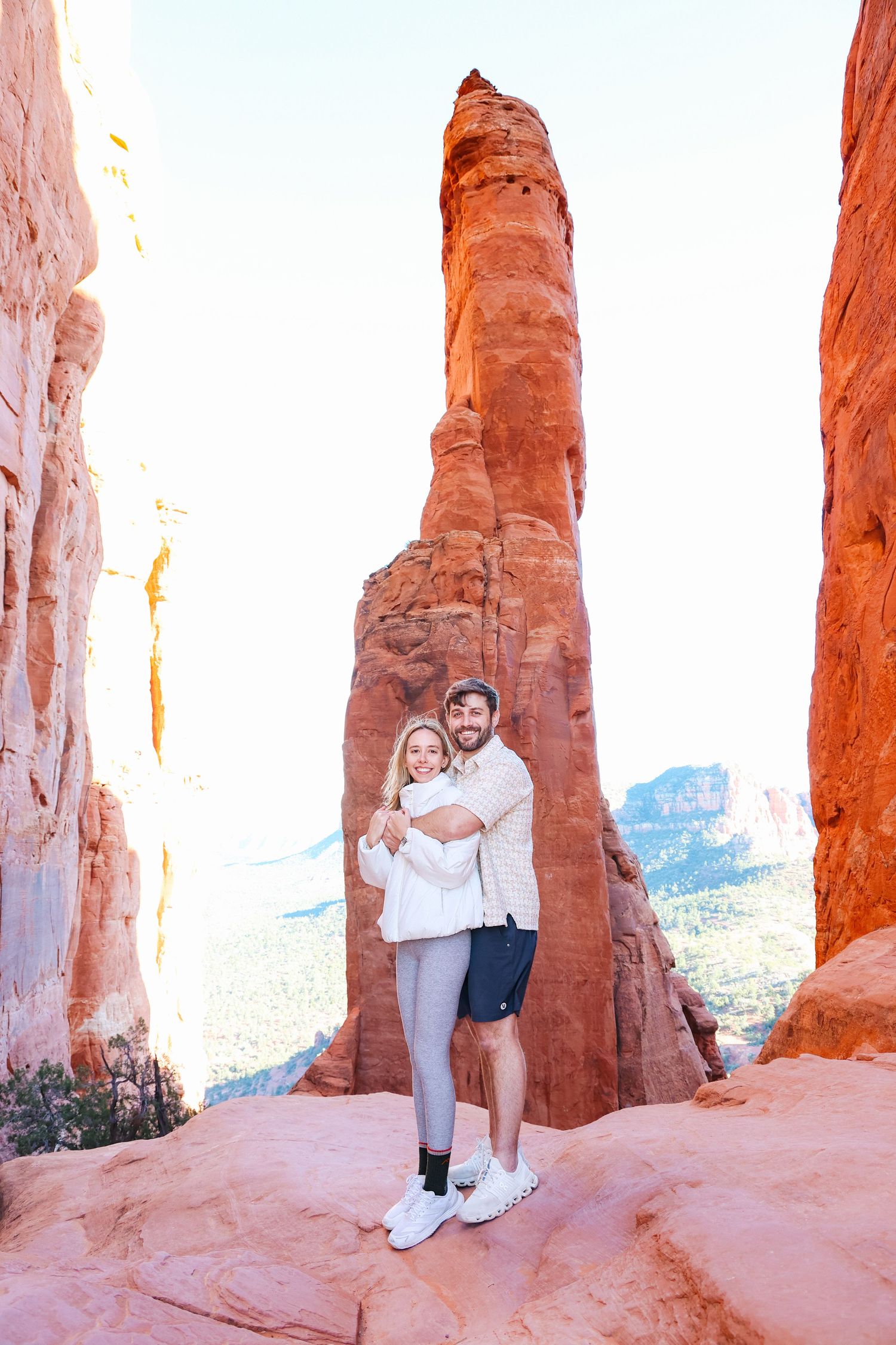 Romantic couple poses against majestic red rock formations at Cathedral Rock Sedona in warm sunlight.