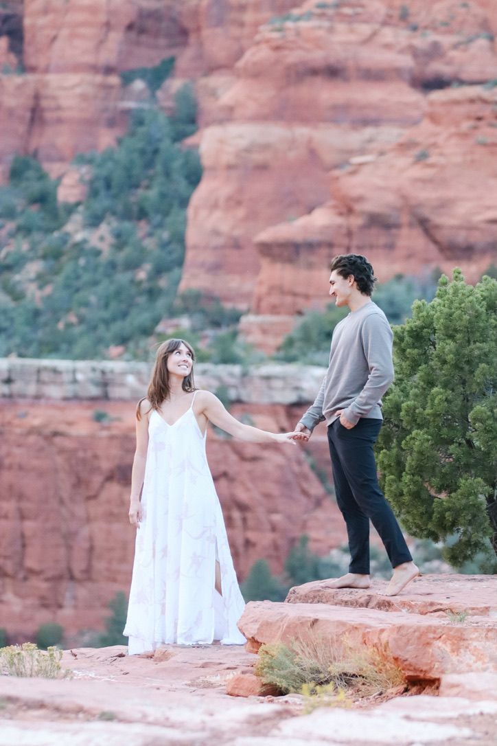 A couple in casual and formal attire standing on red rocks with desert cliffs behind them in Sedona Arizona.