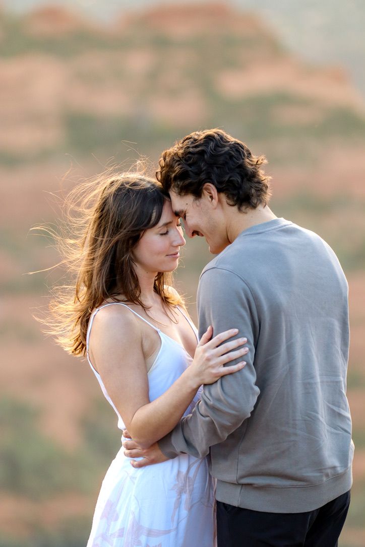 Couple in white dress and grey sweater share romantic moment on desert overlook in Sedona Arizona.