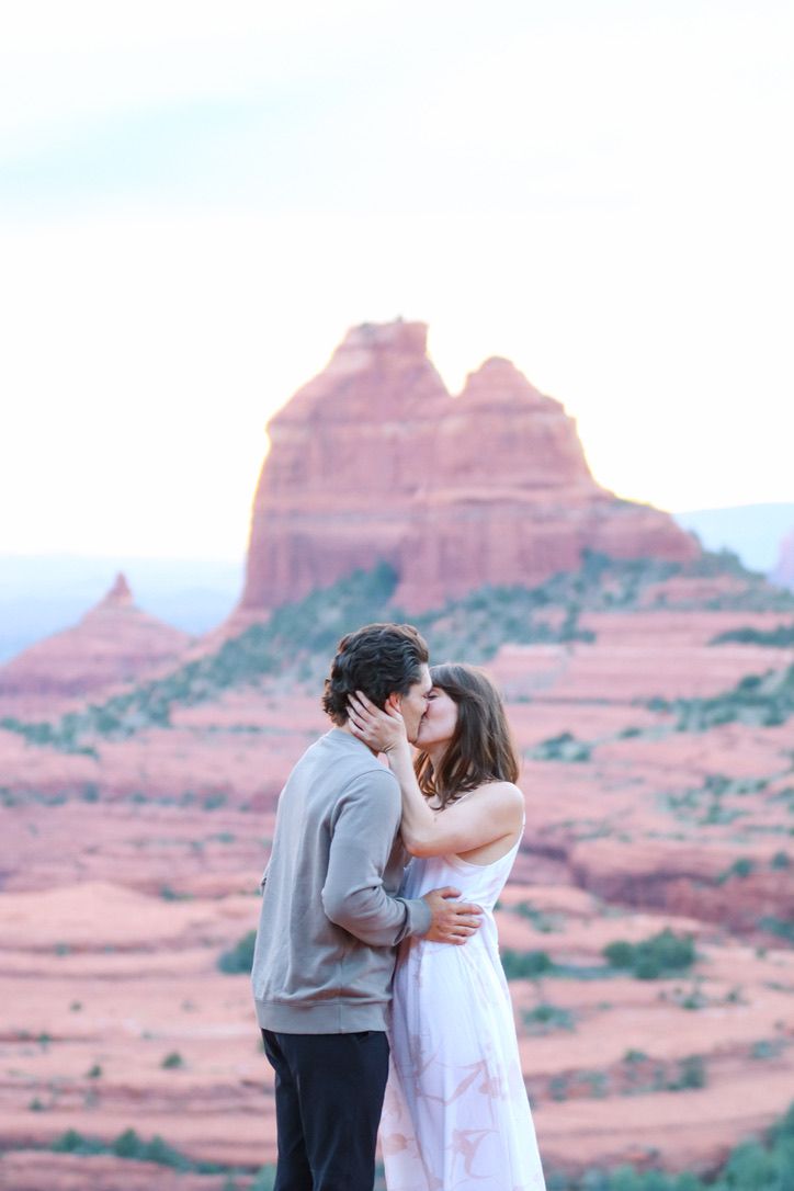 Two people share a romantic moment with Sedona's iconic red rock formations creating a stunning backdrop.