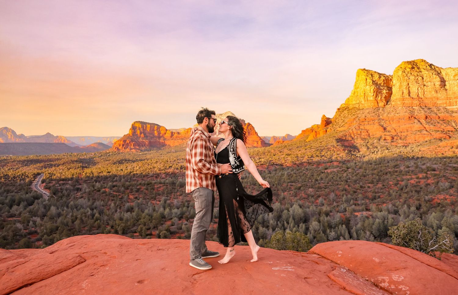 Playful couple poses on red rocks during golden hour in desert landscape in Sedona Arizona.