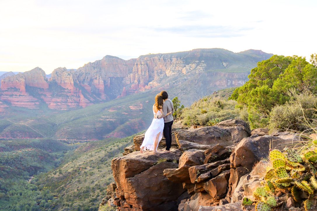 Two people on a rocky overlook with sweeping views of red rock canyons and mountains in Sedona Arizona.