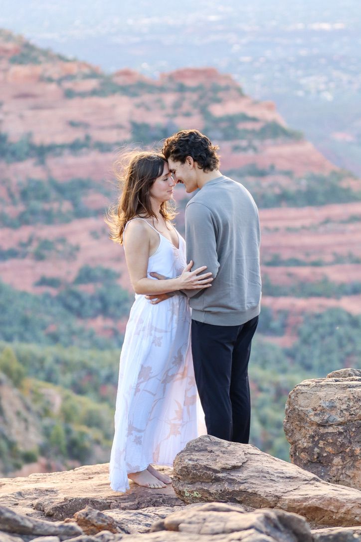 A tender embrace on rocky terrain with red sedimentary cliffs in the background in Sedona Arizona.