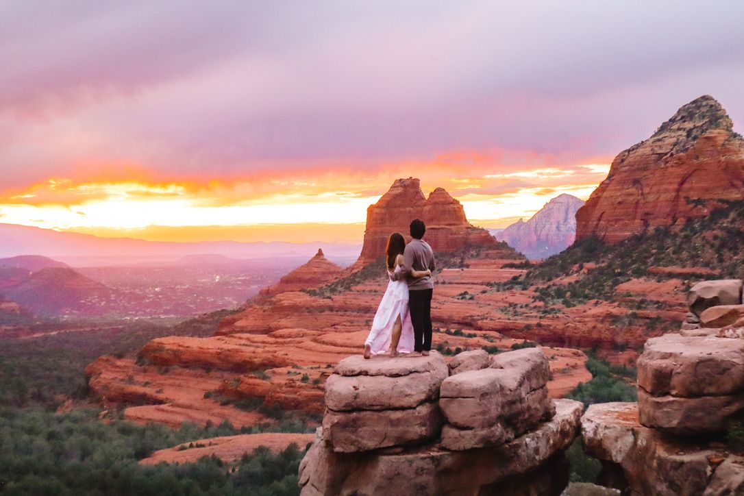 A romantic couple embraces on red rocks at sunset in Sedona with dramatic mountain views in the background in Sedona Arizona.