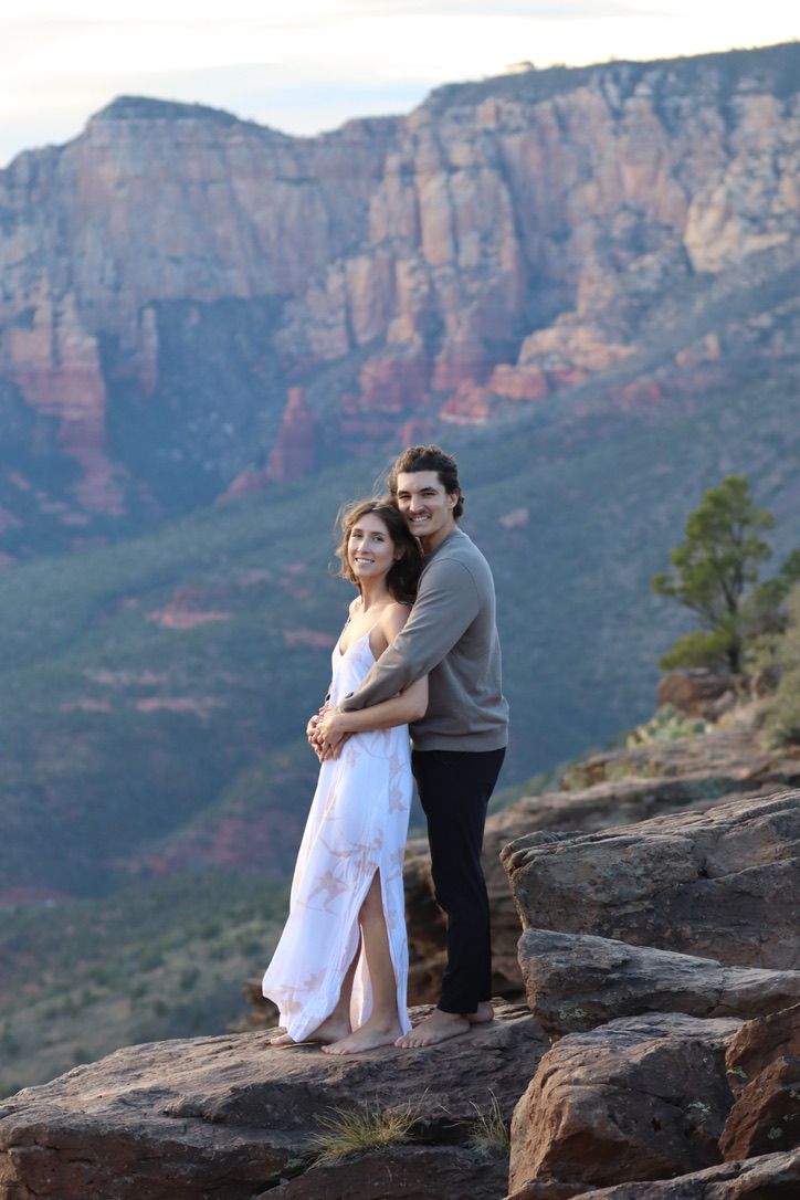 A couple shares a romantic moment on a cliff edge overlooking red rock canyons in Sedona Arizona.
