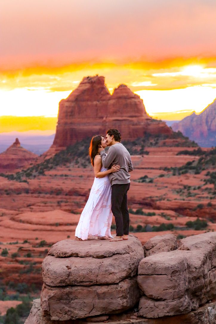 Couple kisses on red rock formation with red rock backdrop in Sedona at sunset.