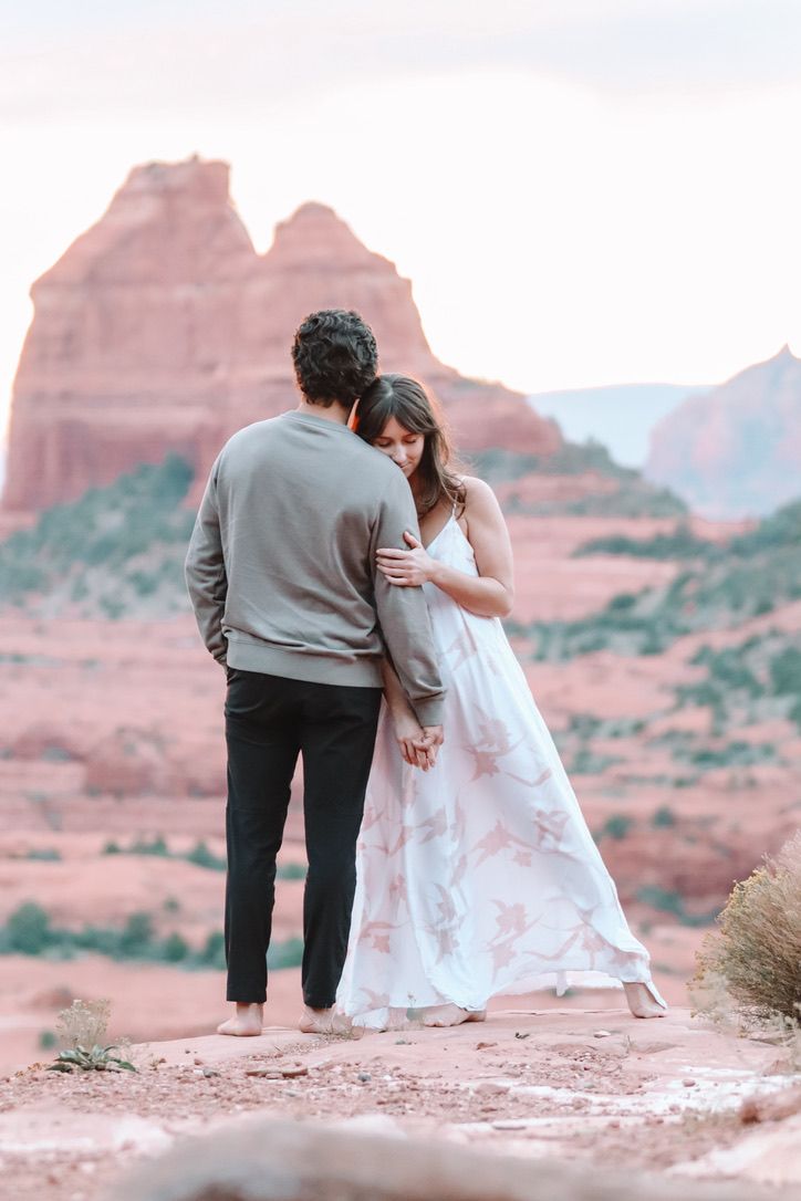 Two people embrace while standing on desert rocks during golden hour in Sedona Arizona.
