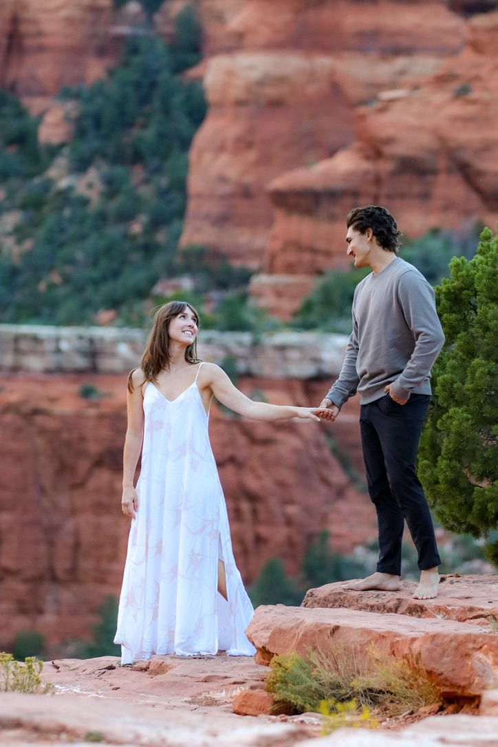 Two people share playful moments on red rock formations overlooking a desert canyon in Sedona Arizona.