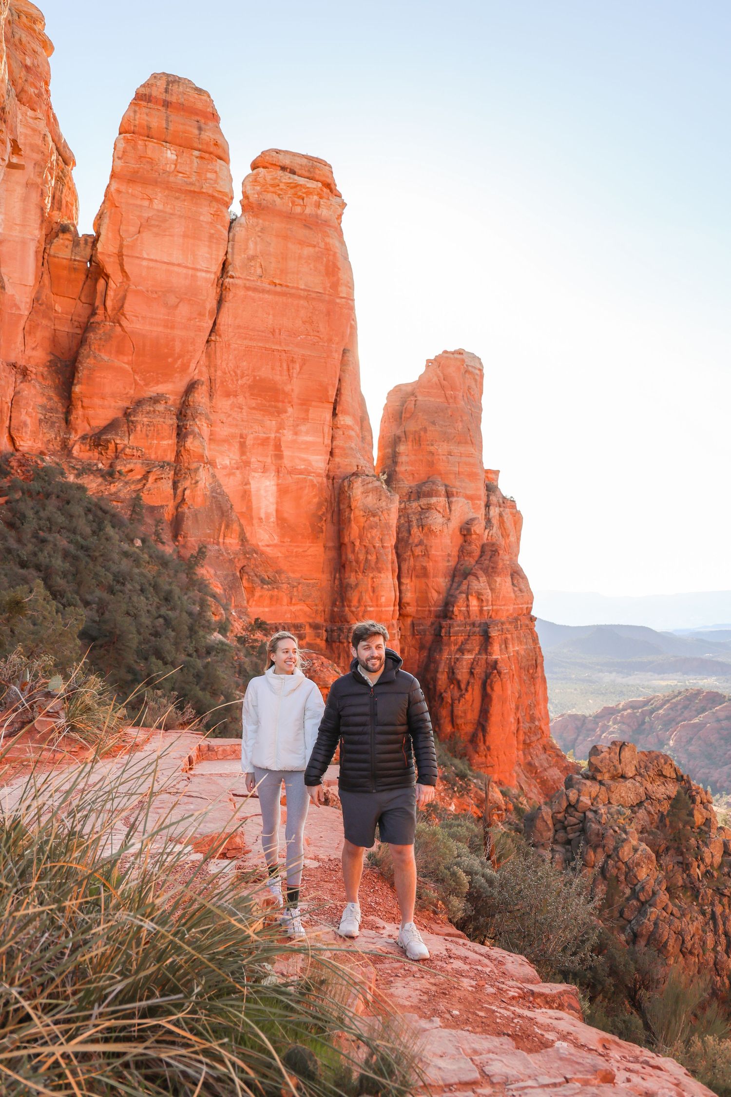 Hikers stand on red rock formations at Cathedral Rock in Sedona during golden hour against a scenic desert landscape.