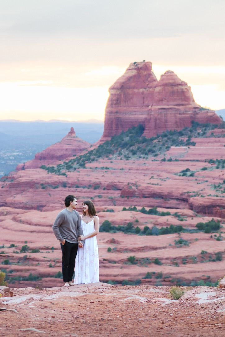 A couple stands together on red rocks with towering Sedona formations in the background.
