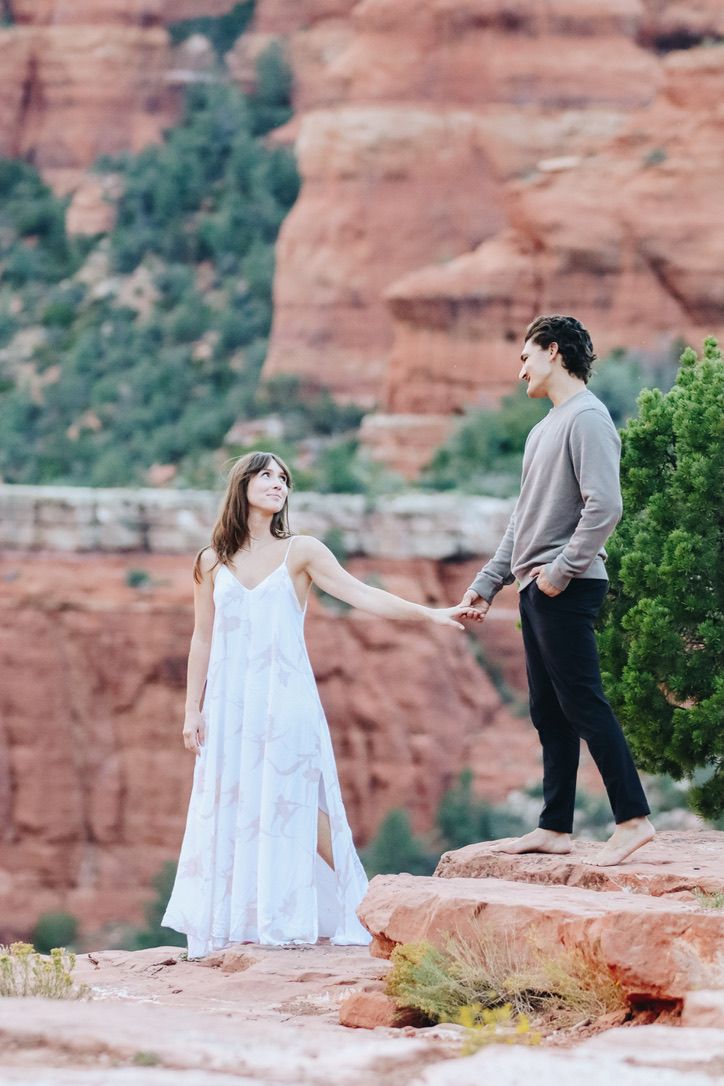 A couple standing on desert rocks with dramatic red cliff formations in the background in Sedona Arizona.