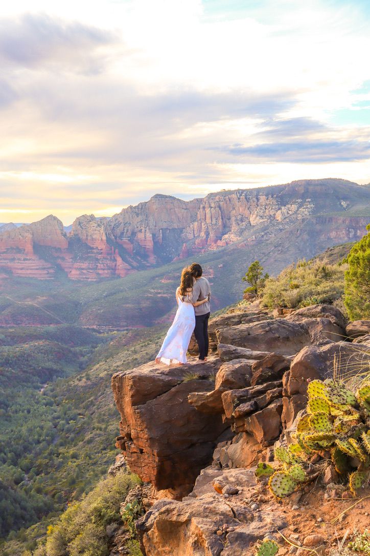 Two people sit together on a cliff edge overlooking a vast canyon landscape at sunset in Sedona Arizona.