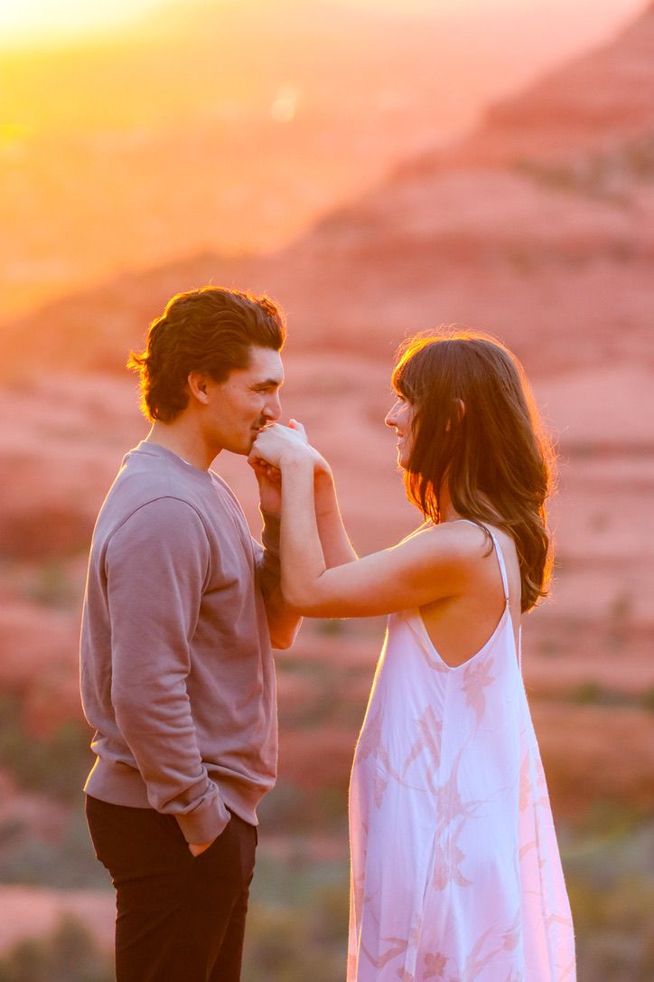 A couple shares an intimate moment at sunset against a warm orange sky in Sedona Arizona.